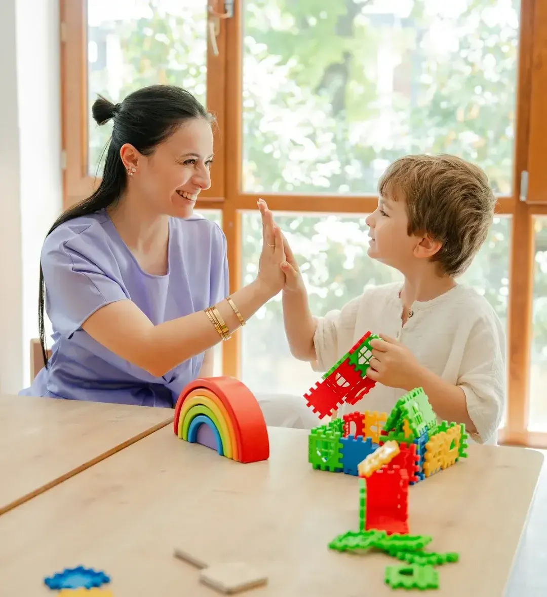 A mother and her son giving each other a high five over a block tower