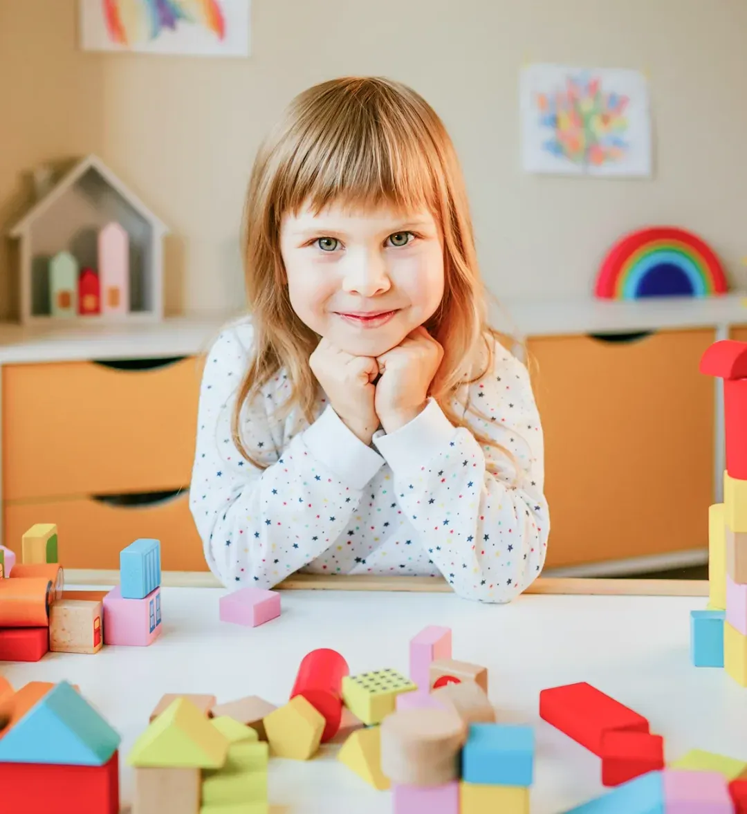 Smiling girl at a table full of colourful wooden blocks
